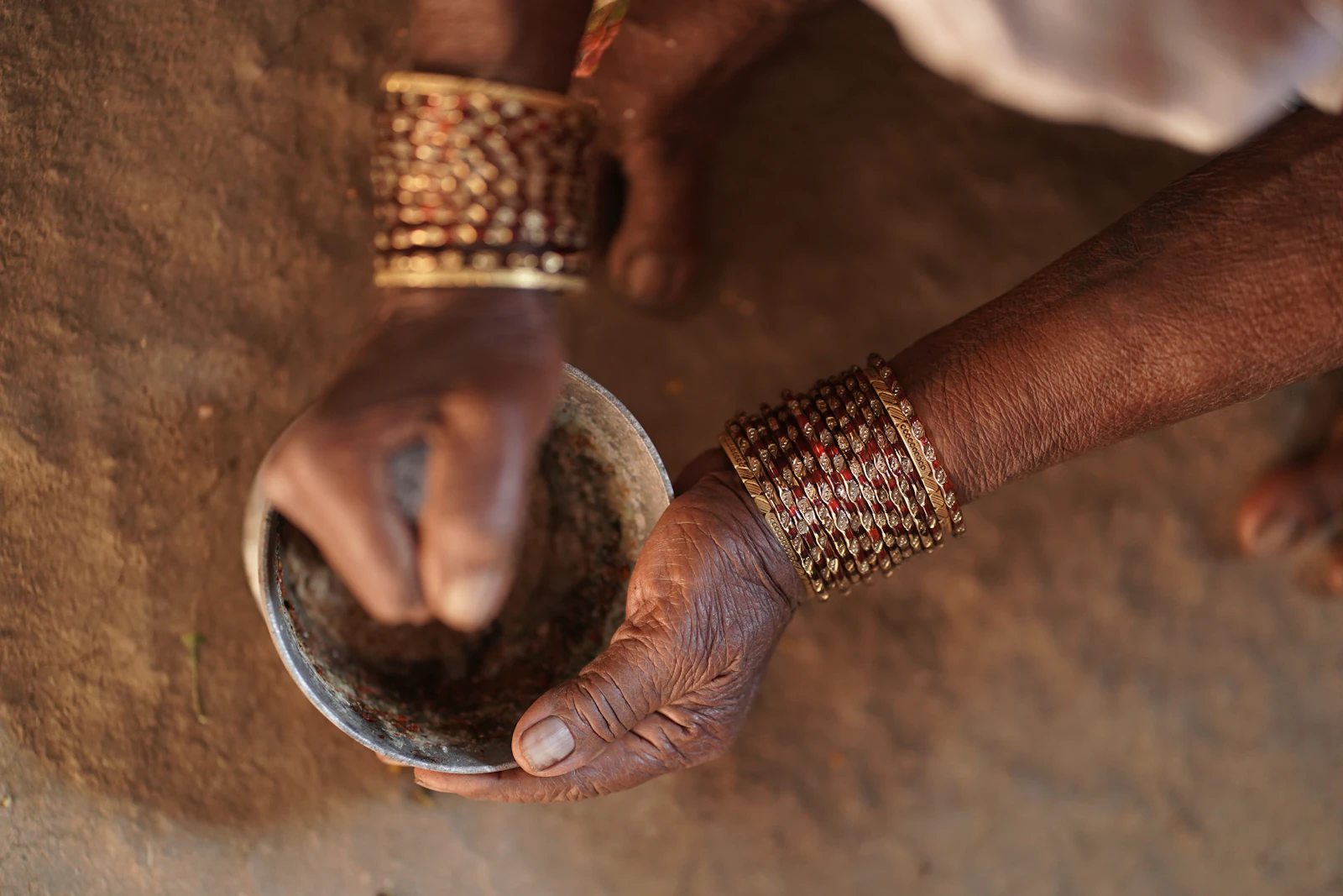 Hands wearing traditional bangles grinding herbs in a stone bowl